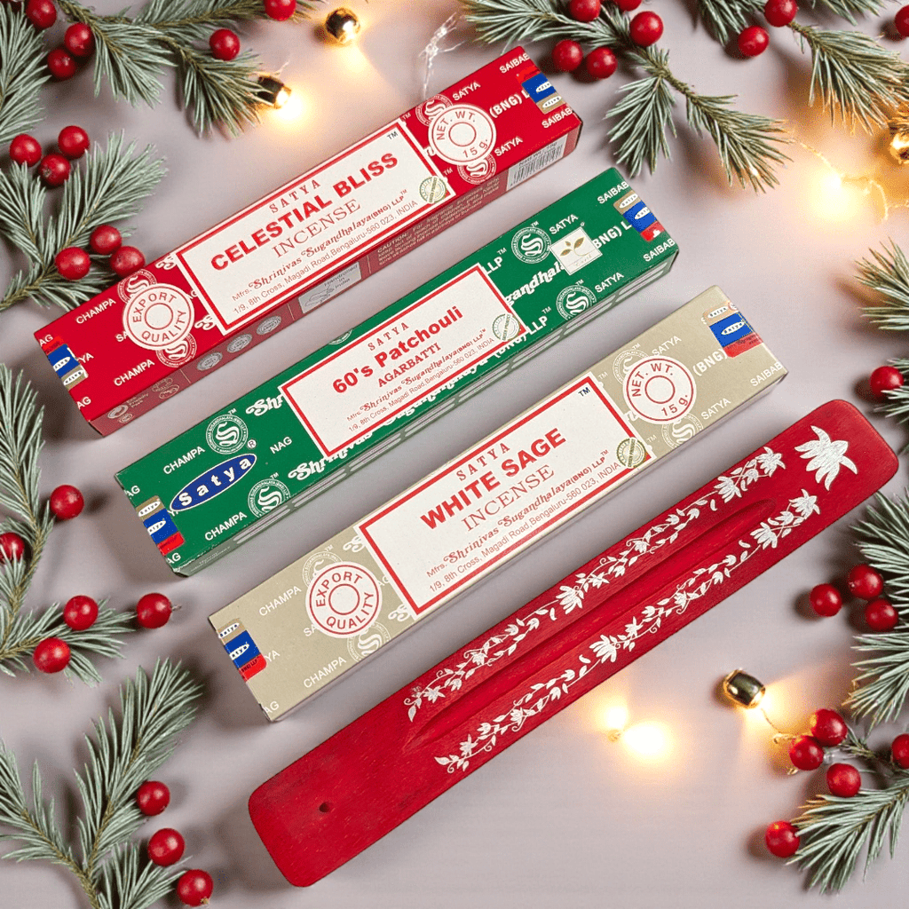 Three Satya incense boxes with a red holder on a decorative background with pine branches and red ornaments. Available at Zen Collection Metaphysical Stores Near Me Barrie