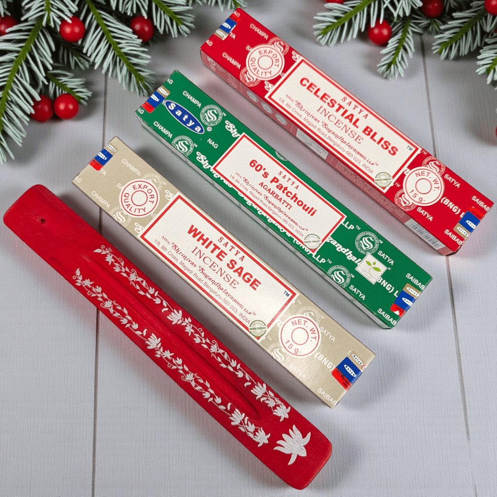 Three Satya incense boxes with a red holder on a decorative background with pine branches and red ornaments. Available at Zen Collection Metaphysical Stores Near Me Barrie