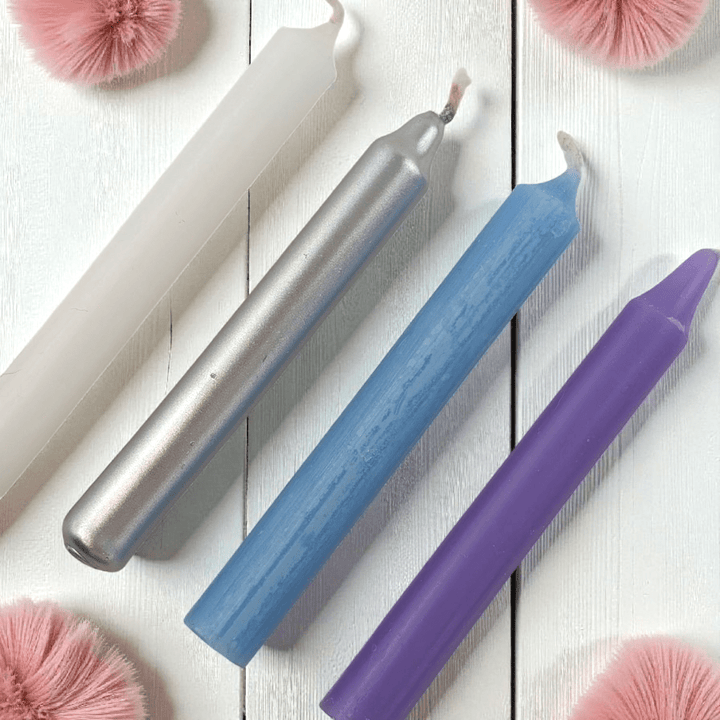 Three colorful spell candles (silver, blue, purple) on a white wooden surface with pink decorative elements. Shop In-Store at our crystal store near me or online 24/7