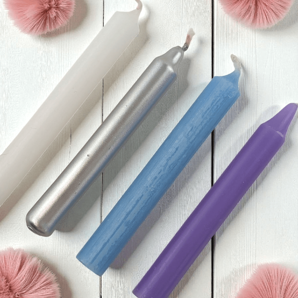 Three colorful spell candles (silver, blue, purple) on a white wooden surface with pink decorative elements. Shop In-Store at our crystal store near me or online 24/7