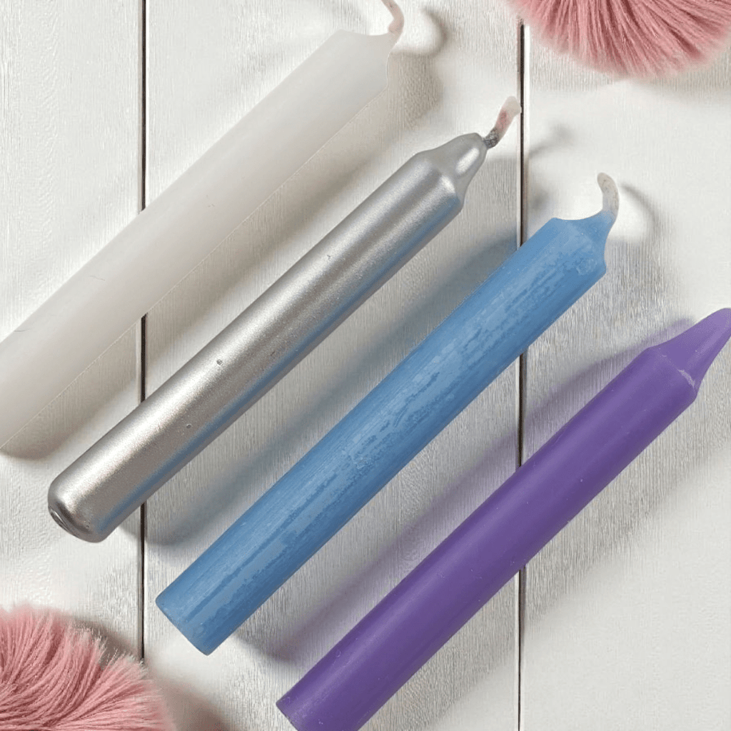Three colored spell candles (silver, blue, purple) on a white wooden surface with pink fluffy objects. Shop in-store at our metaphysical store in Barrie or online 24/7