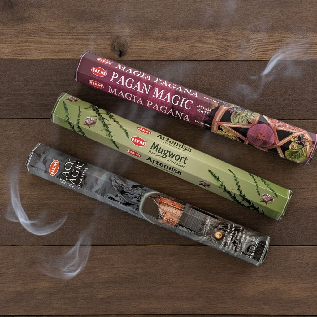 Three packs of HEM incense sticks on a wooden surface with smoke rising. available at zen collection crystal stores barrie