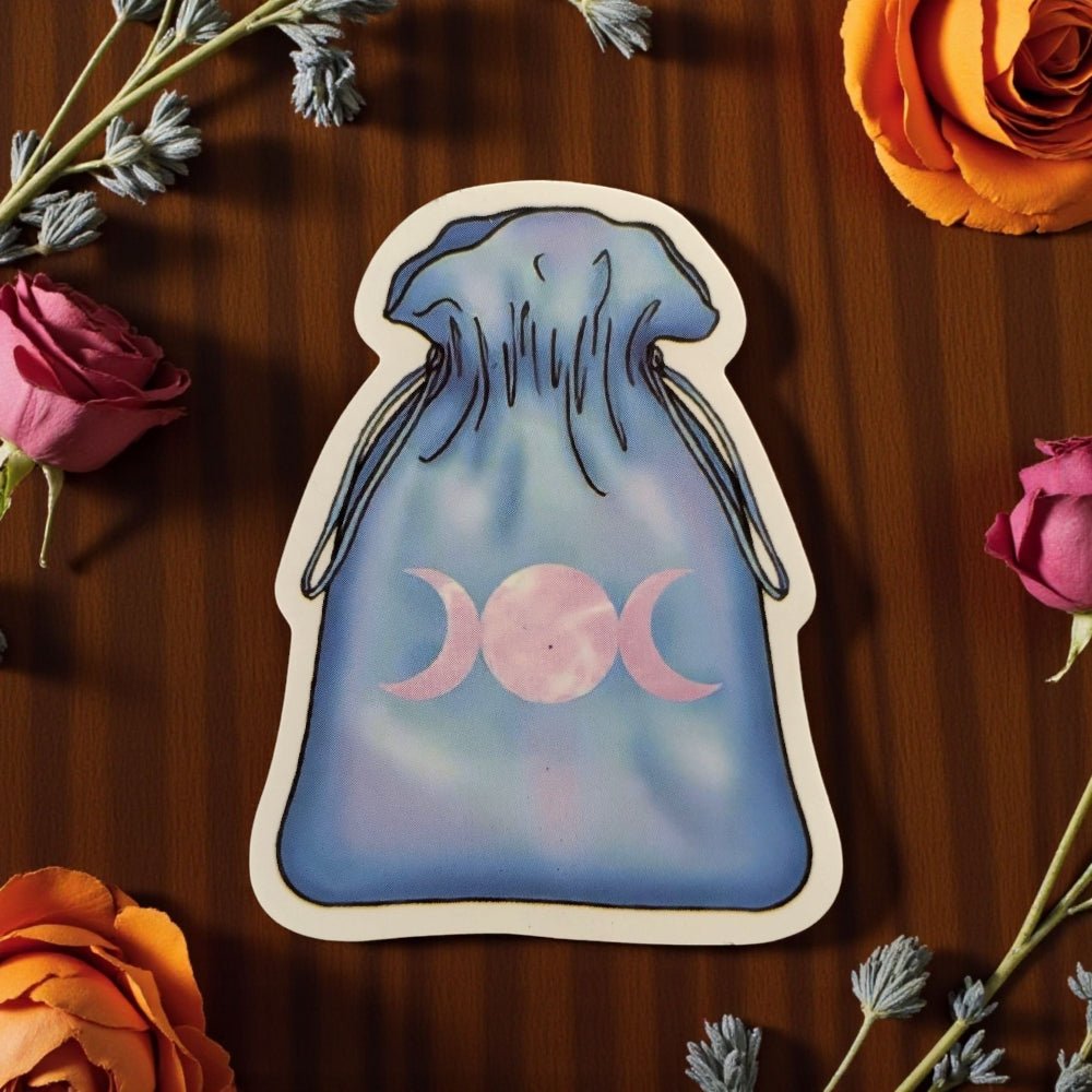 Sticker of a blue bag with a pink moon symbol on a wooden surface with flowers witchs crystal set available at zen collection crystal stores in barrie