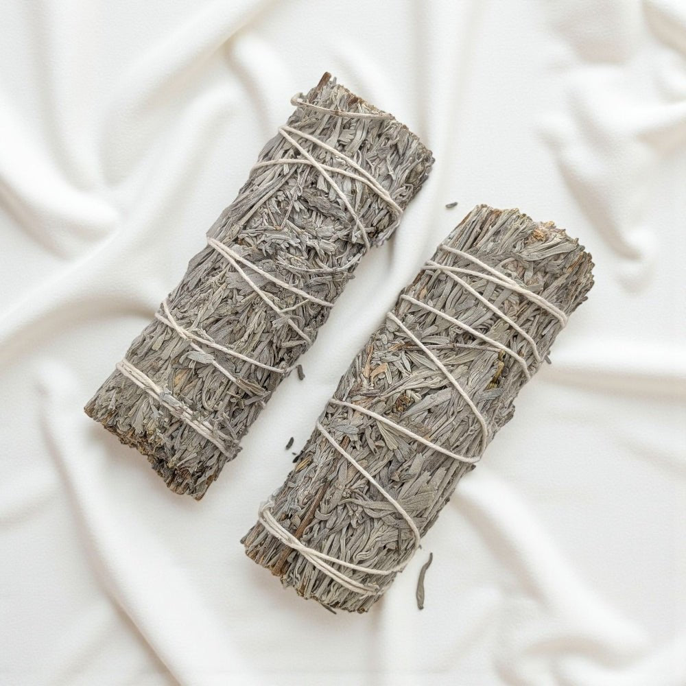 Two blue sage smudge sticks tied with string on a light fabric background. available now at zen collection metaphysical store