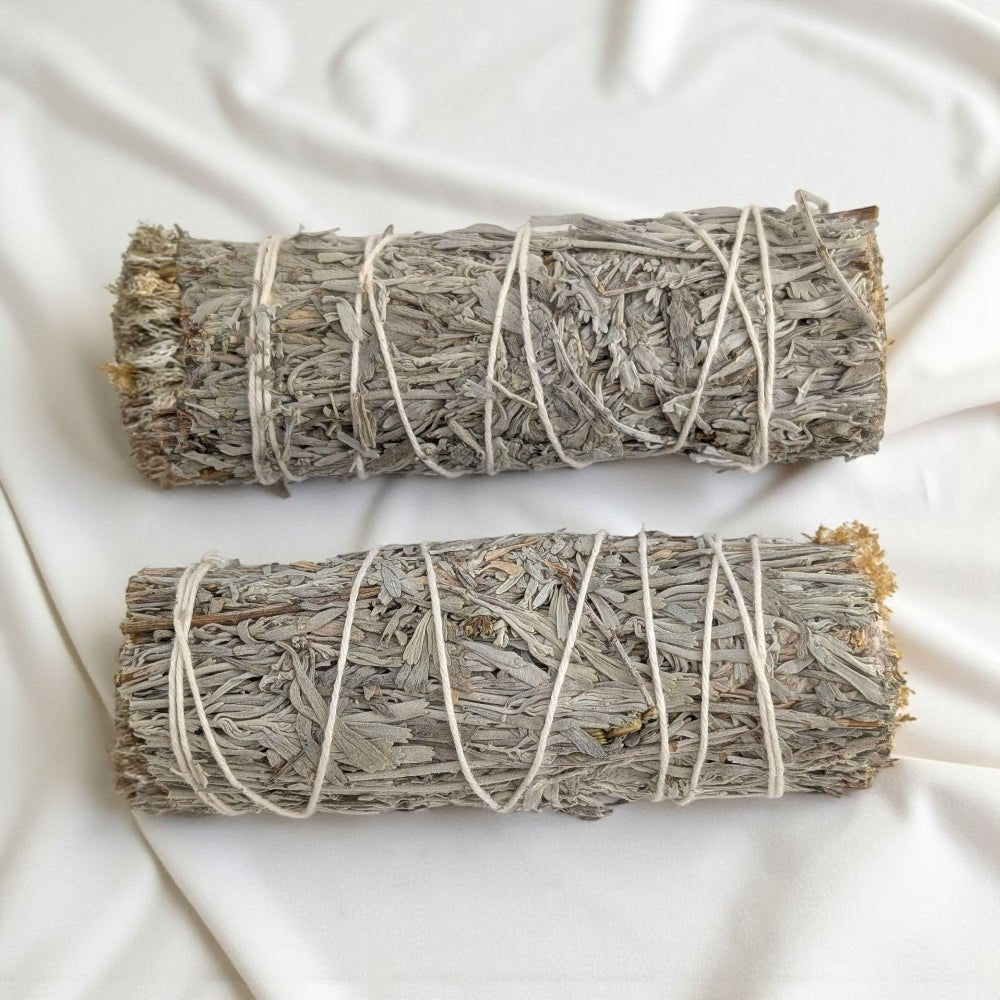 Two bundles of blue sage wrapped in twine on a white fabric background available at zen collection metaphysical store in barrie ontario