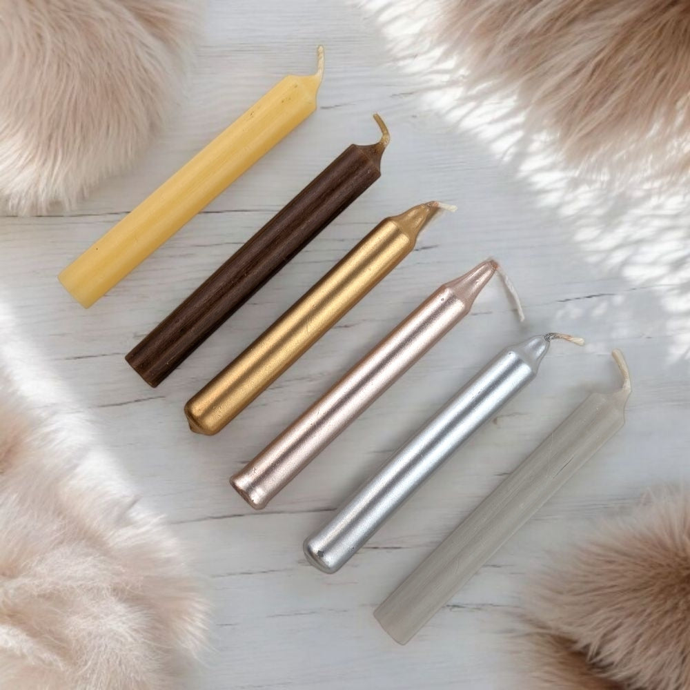 Set of five chime candles in gold, bronze, silver, and rose gold on a light wooden surface with fur accents. available online or instore at Barrie's metaphysical store
