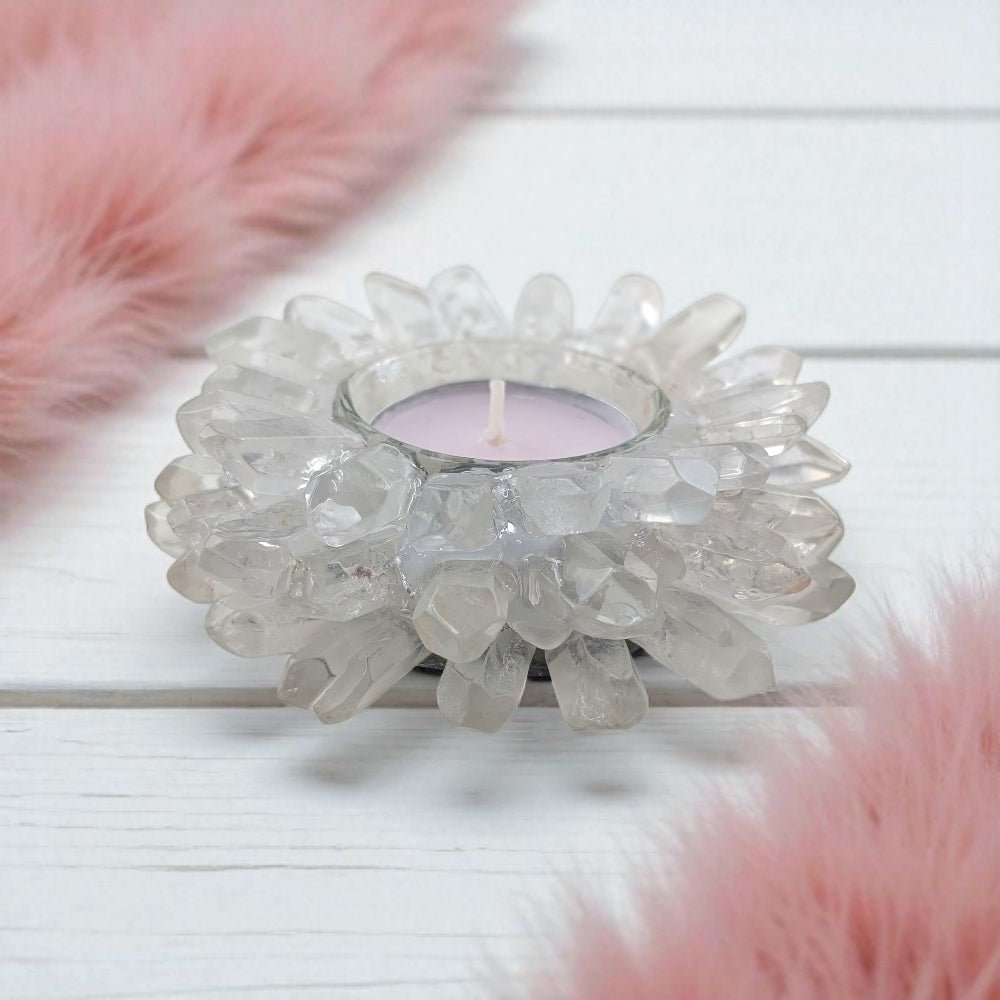 Clear Quartz crystal candle holder with a lcandle on a white surface with pink fluffy objects.