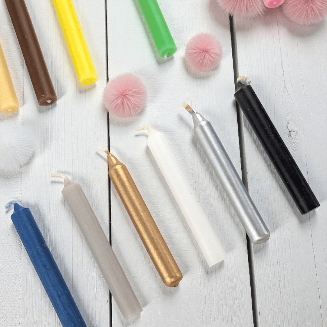 Colorful spell candles on a white wooden surface with decorative pom-poms. Available in store or online at zen collection crystal stores barrie