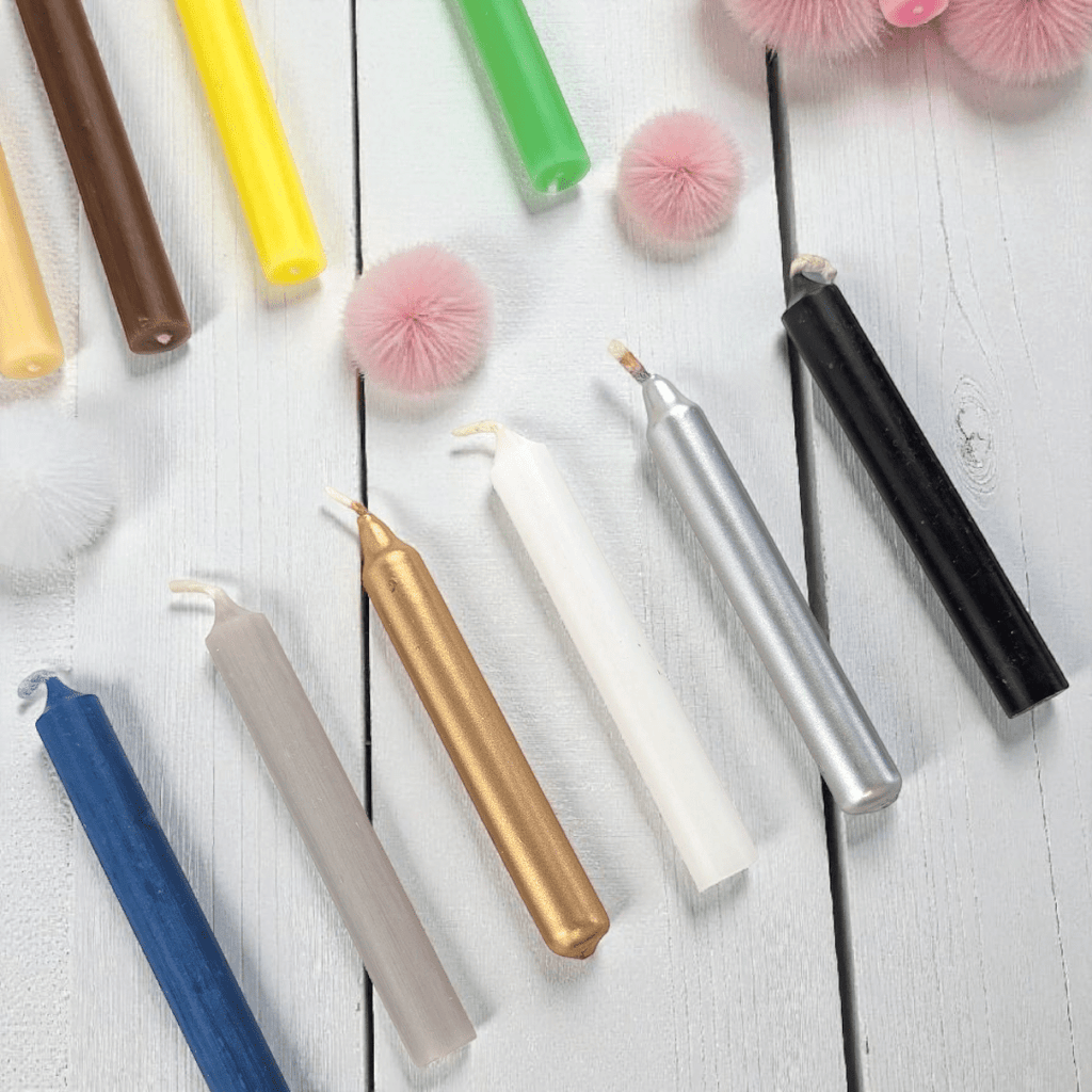 Colorful spell candles on a white wooden surface with decorative pom-poms. Available in store or online at zen collection crystal stores barrie