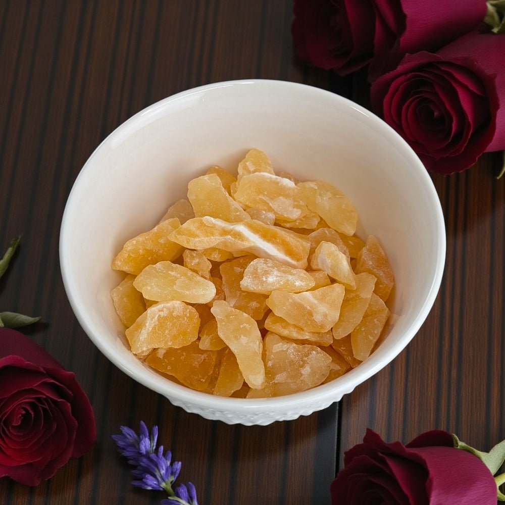 Sacral Chakra Crystals - White bowl filled with Orange Calcite Crystal pieces on a wooden surface with red roses and lavender. Available at Zen Collection Crystal Stores Barrie
