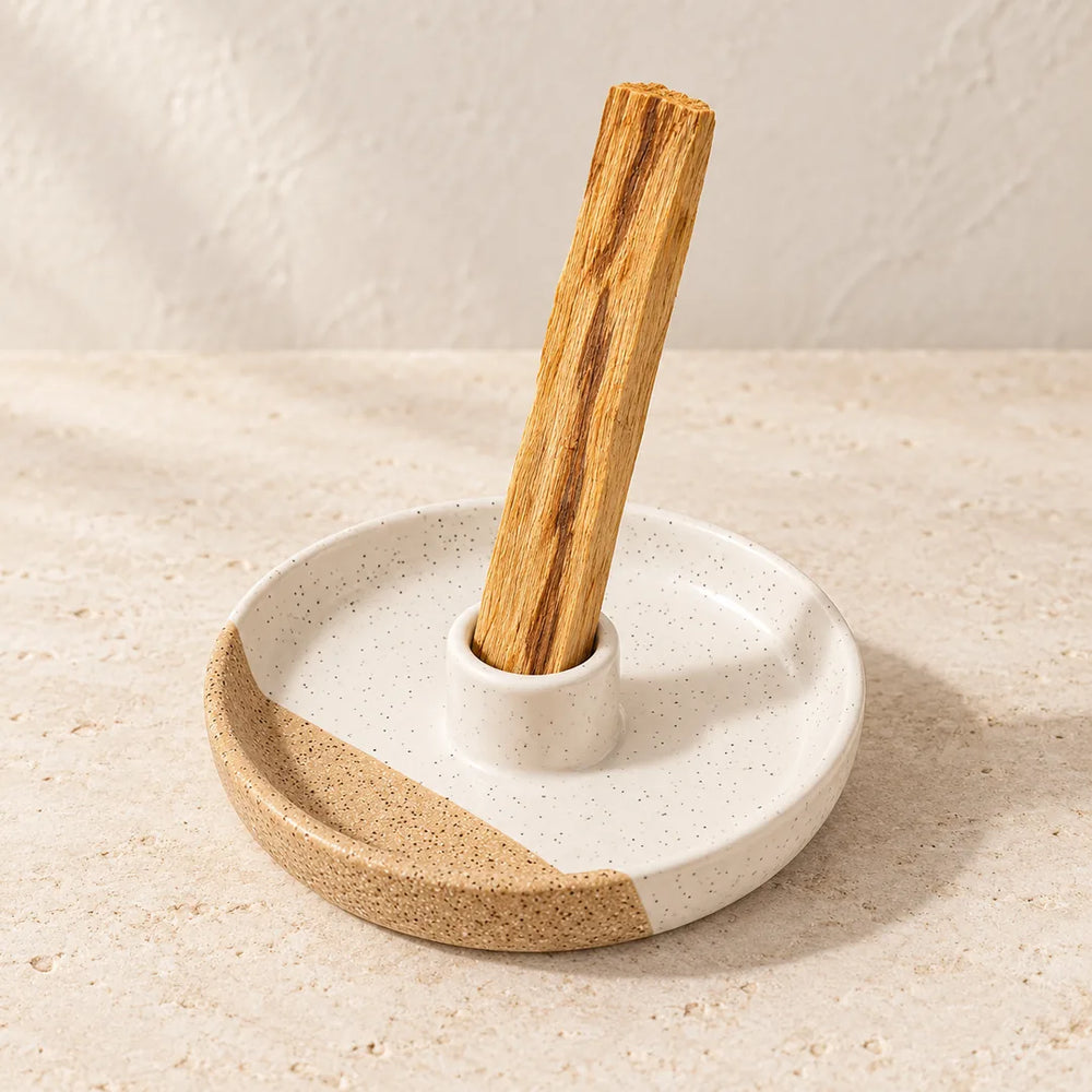 A single Palo Santo stick standing in a speckled ivory and sand ceramic holder on cream stone; holder sold separately.