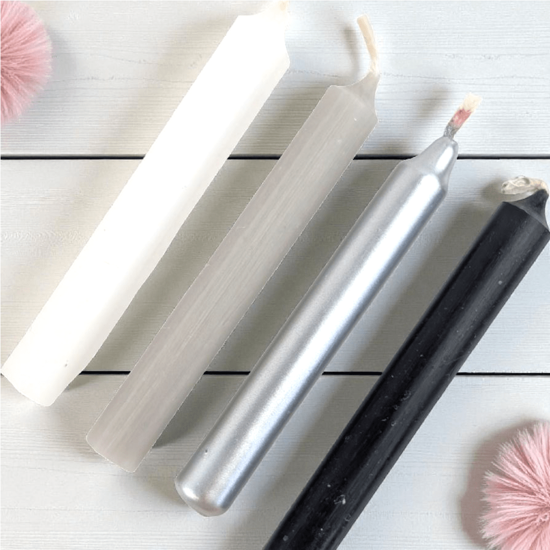 Set of four metallic spell candles on a light wooden surface with pink decorative elements. shop in-store at our metaphysical shop in barrie or online 24/7