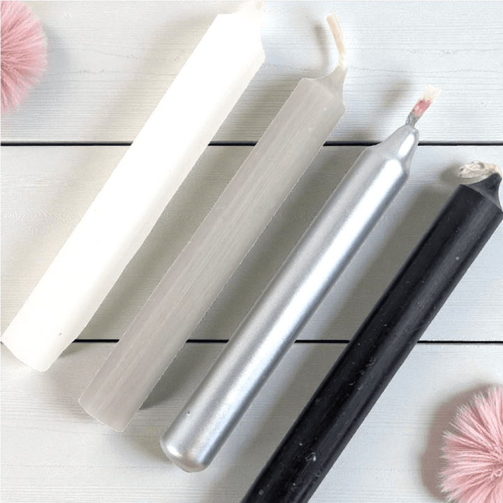Set of four metallic spell candles on a light wooden surface with pink decorative elements. shop in-store at our metaphysical shop in barrie or online 24/7