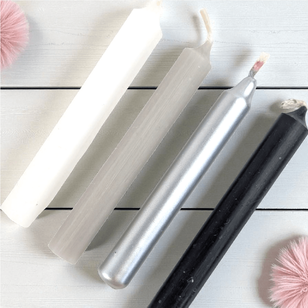 Set of four metallic spell candles on a light wooden surface with pink decorative elements. shop in-store at our metaphysical shop in barrie or online 24/7