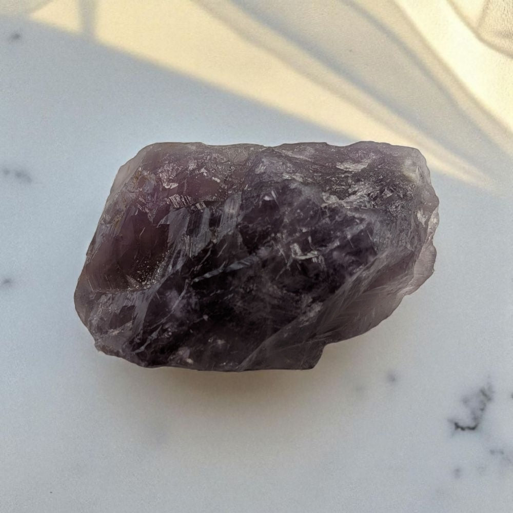 Raw purple crystal on a marble surface