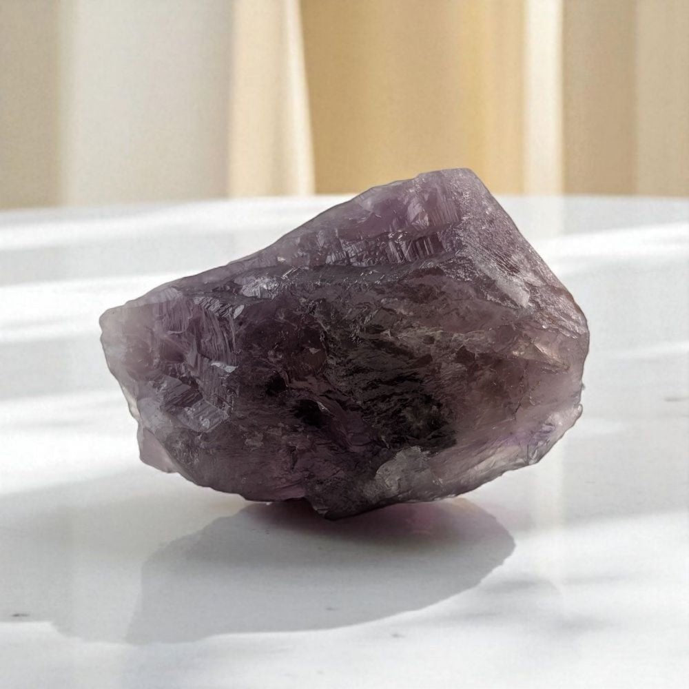 Raw amethyst crystal on a white surface with a neutral background