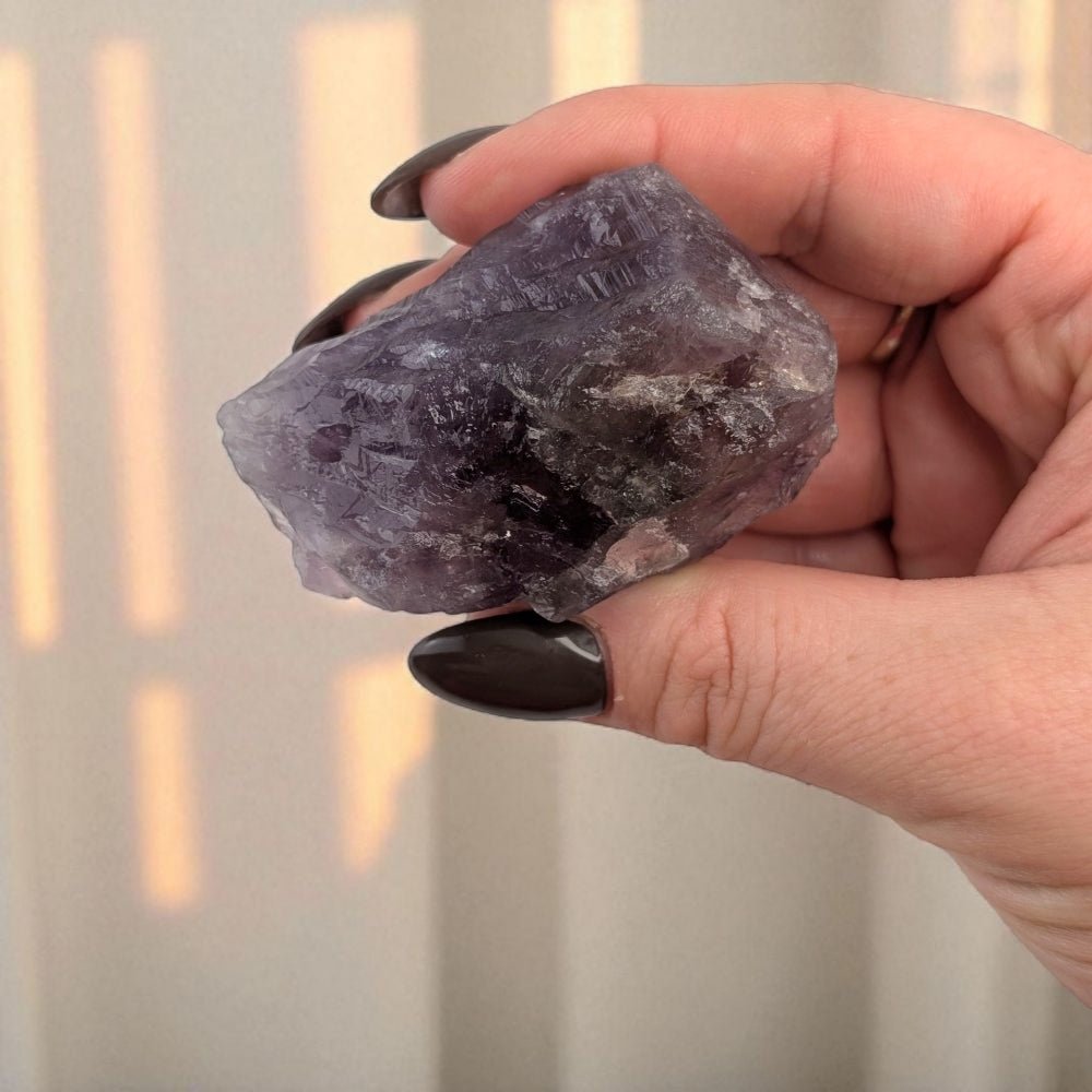 Hand holding a purple crystal against a neutral background