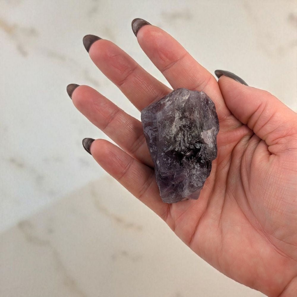 Hand holding a purple amethyst crystal against a marble background