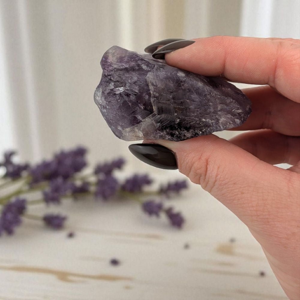 Hand holding a purple crystal with lavender flowers in the background