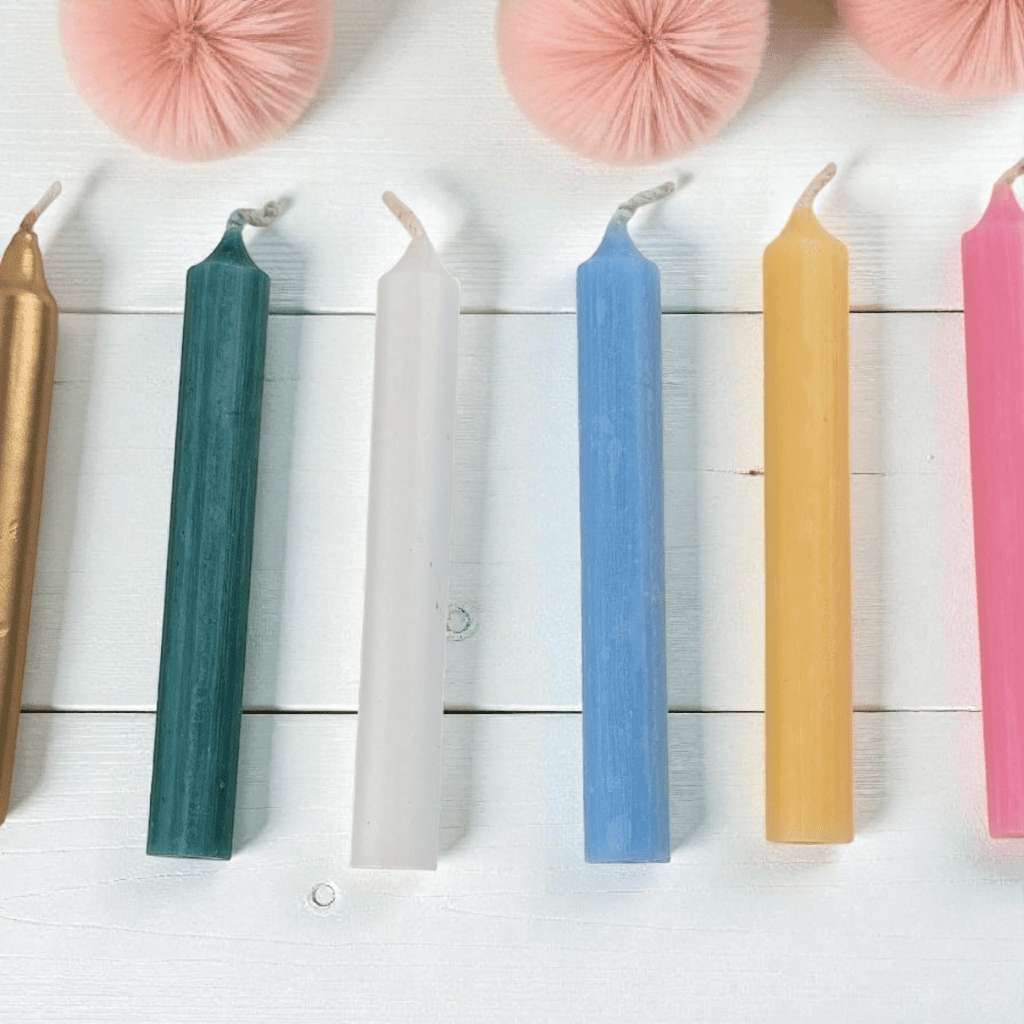 Colorful spell candles on a white wooden surface with pink decorative elements available at zen collection metaphysical store in Barrie