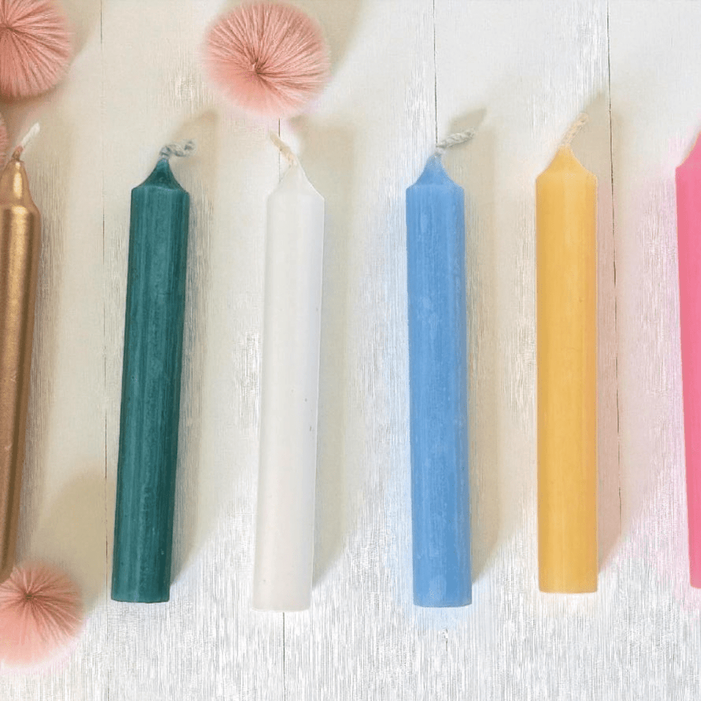 Colorful spell  candles on a textured white surface with decorative pink pom-poms. Available at Zen Collection metaphysical store Barrie