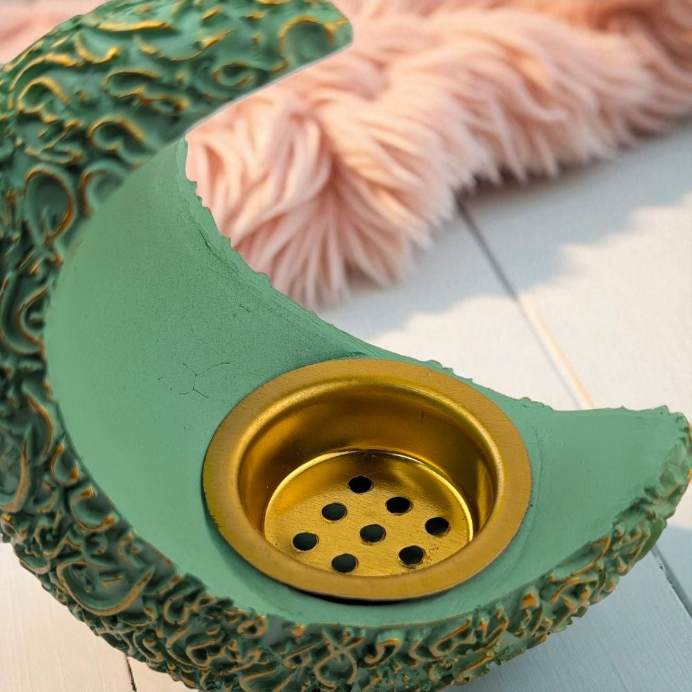 Decorative green and gold resin burner resembling a crescent moon on a light wooden surface.